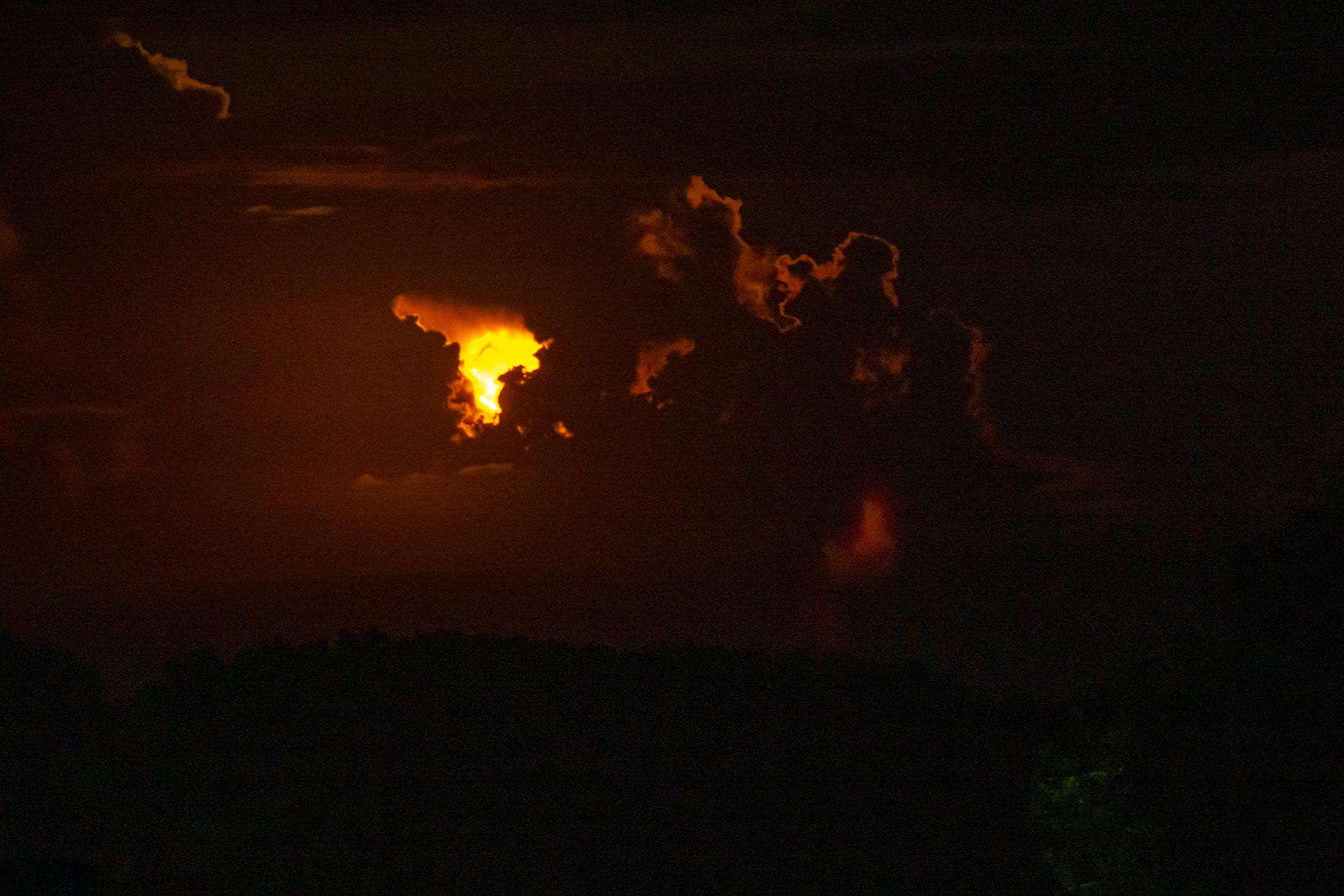 暗闇の中、雲間からオレンジ色に輝く月が姿を現している夜空