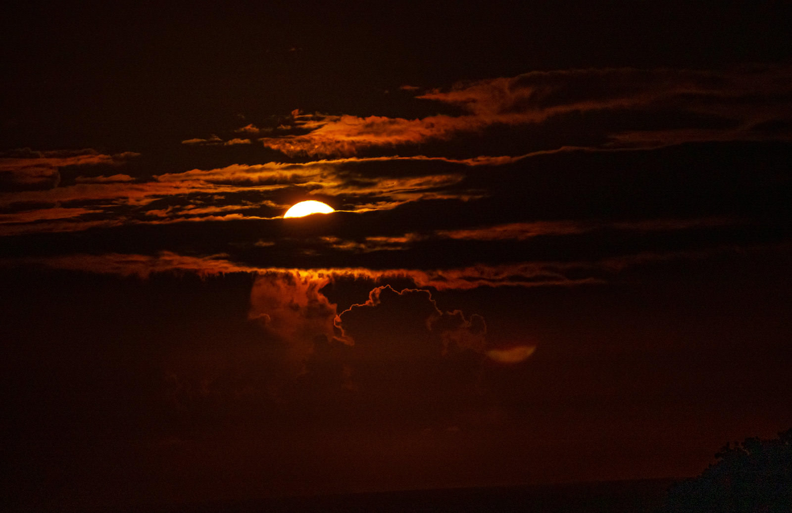 オレンジや赤の夜空で雲間から光る満月が雲を照らす様子