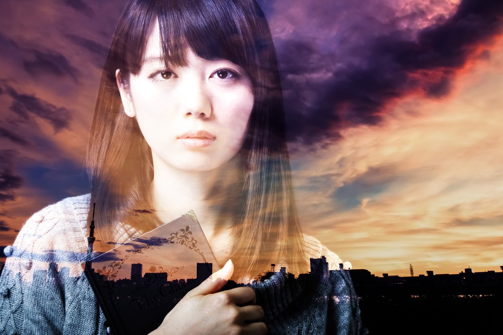 夕焼けを背景に本を握りしめて遠くを見つめる女性のフォトモンタージュ［モデル：モデルリリース］