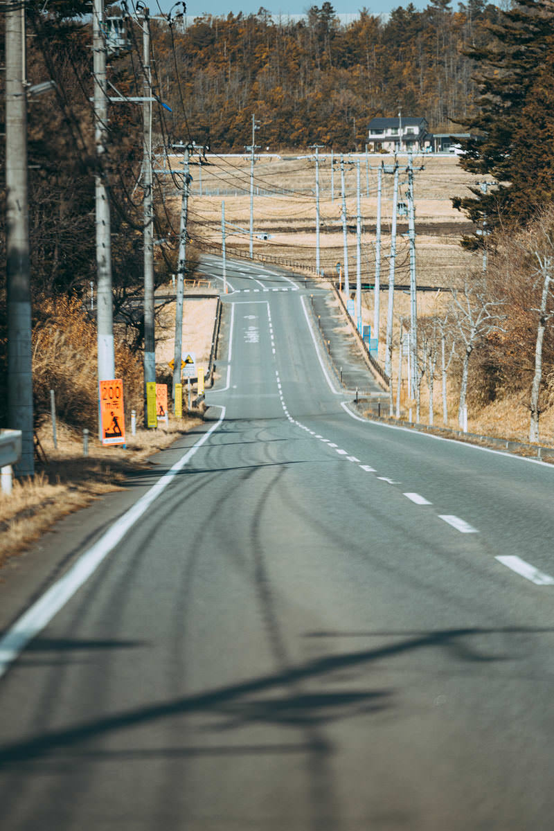福島県浜通りの工事現場が見える下り坂。両側に電柱が並ぶ道路の先に建設中の施設が見える。