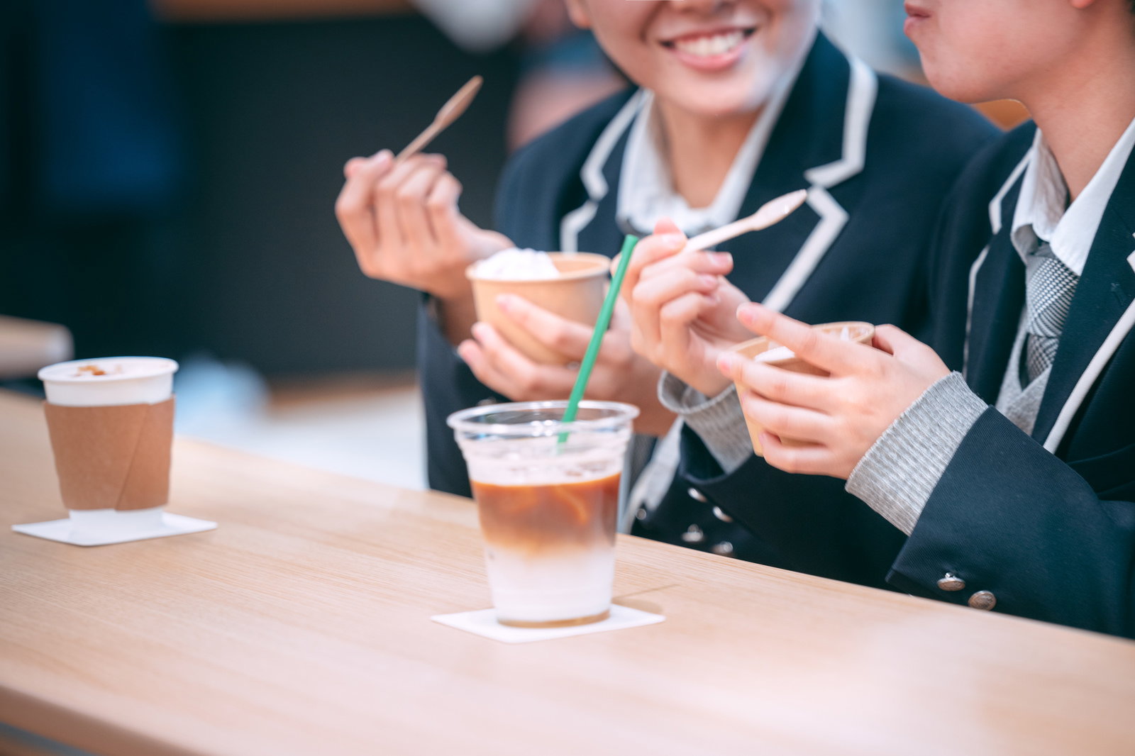 学生服の女子高生がカフェでアイスドリンクを飲みながら談笑している