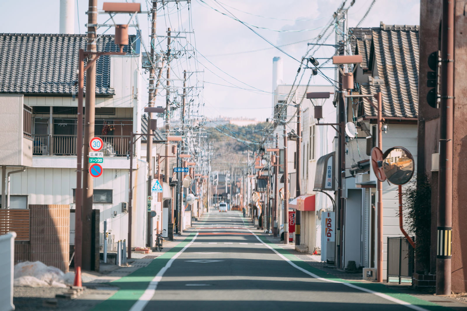 瓦屋根の建物が両側に立ち並ぶ広野町駅前通り。電線が複雑に張られ奥に山が見える。