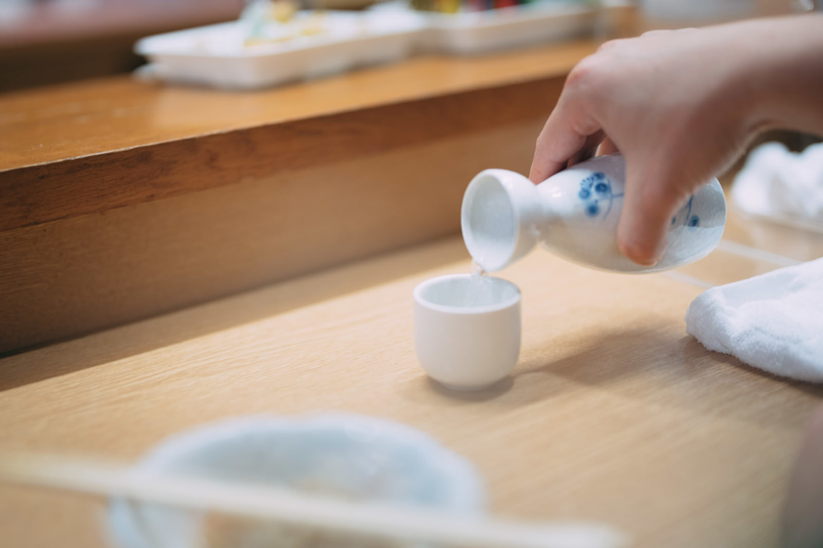 居酒屋の木製テーブルでとっくりからおちょこに熱燗を注ぐ手元