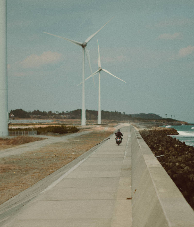 福島県南相馬の右田海岸の防波堤を走るバイカーと背景の風力発電機