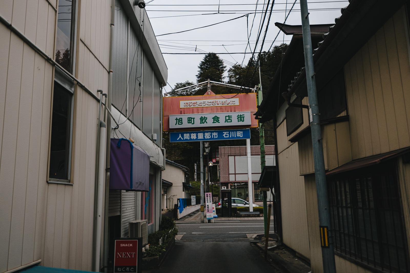 福島県石川町の旭町飲食店街の裏道に立つ複数の看板と両側の店舗