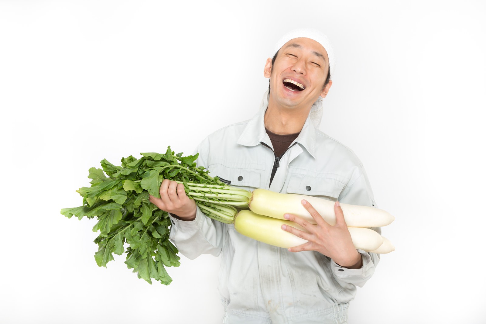 白い作業着姿の男性が、葉付きの大根を両手に抱えて顔を上げ、歓喜の笑みを浮かべている［モデル：大川竜弥］
