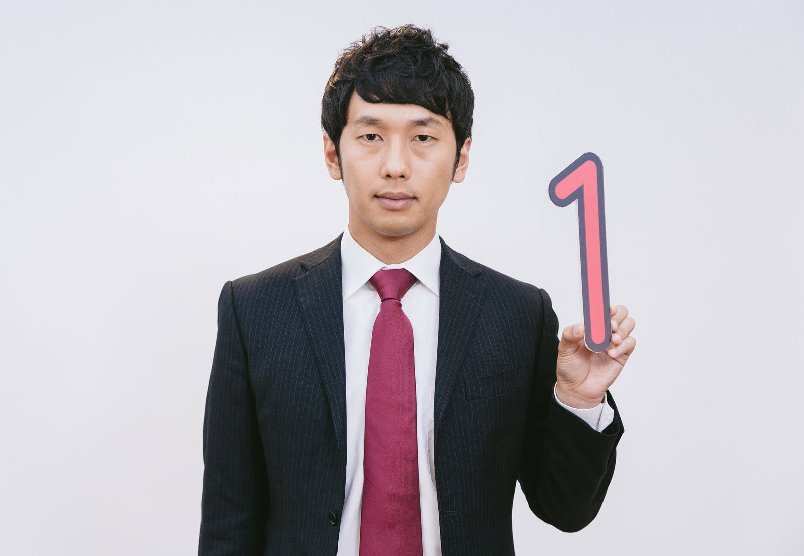 紺ストライプスーツにピンクの「1」を持つ男性が正面を向いている［モデル：大川竜弥］