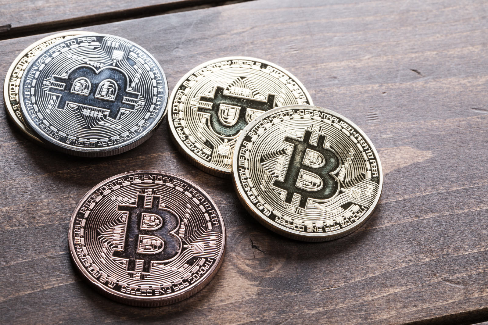 木製テーブルに3枚のビットコインメダルと申告関連書類、スマートフォンが並べられている俯瞰撮影
