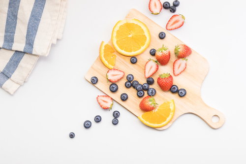 木製のまな板に散らばったカットフルーツとベリー類
