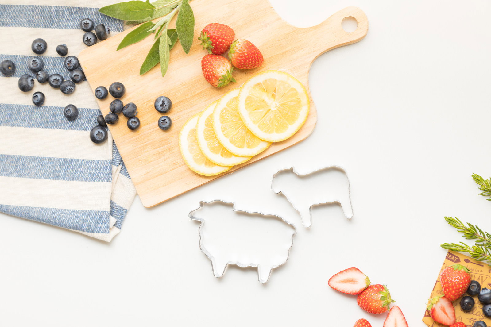 まな板の上にレモンスライス、イチゴ、ブルーベリーと羊のクッキー型が配置されている