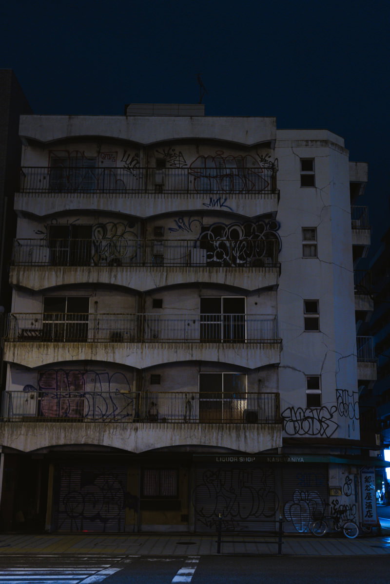 夜の難波の路地裏に建つ雑居ビルの外壁に落書きが描かれている