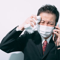 止まらない汗をぬぐいながら通話中の会社員の写真