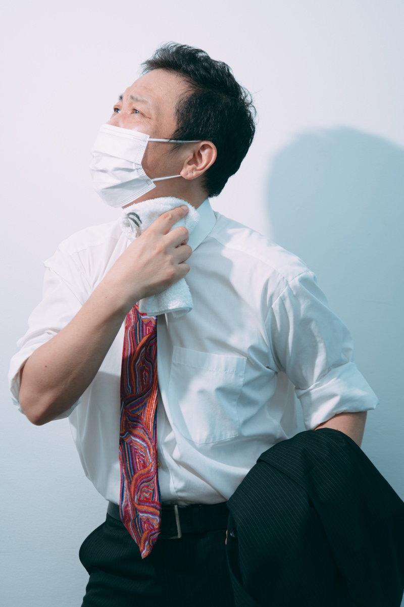 白いワイシャツとネクタイを着た営業マンが暑さで首元の汗を拭いている様子［モデル：のせさん］
