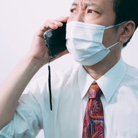 真剣な眼差しで通話するマスク姿の営業マンの写真