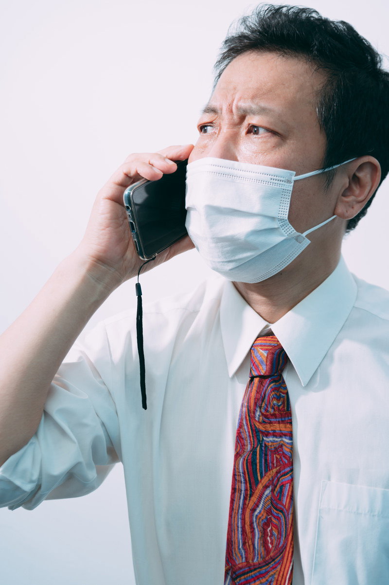 マスクを着けて電話をかける白シャツにネクタイの男性会社員［モデル：のせさん］