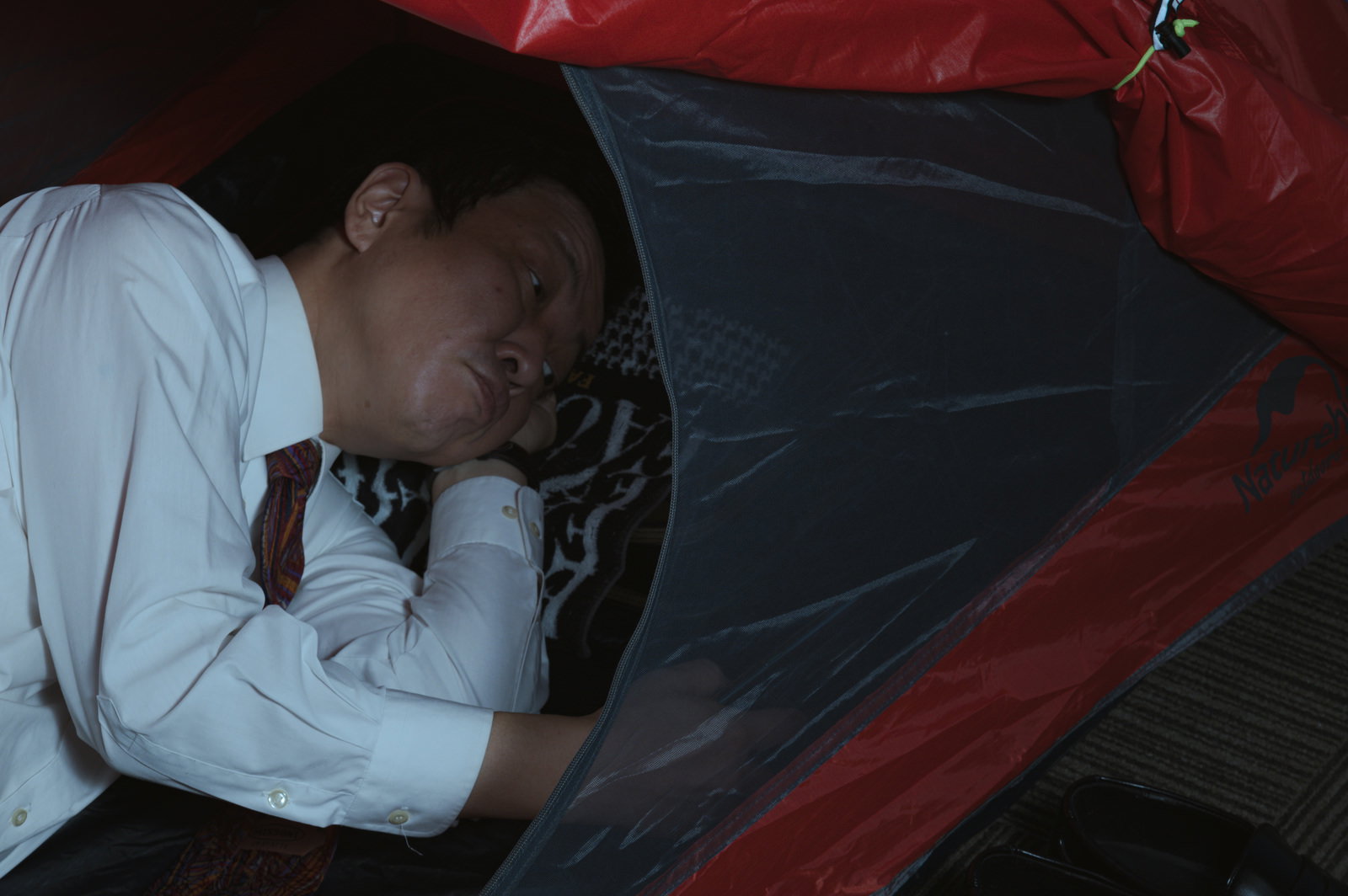 車内で横になって仮眠をとるスーツ姿の営業マン［モデル：のせさん］