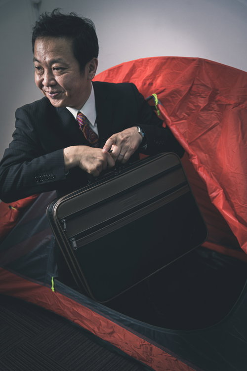 赤い布に包まれたキャリーケースを手にするテントから出勤する営業マン