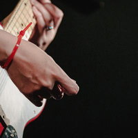 赤い結束バンドを付けて赤いストラトキャスターを弾くギタリストの写真