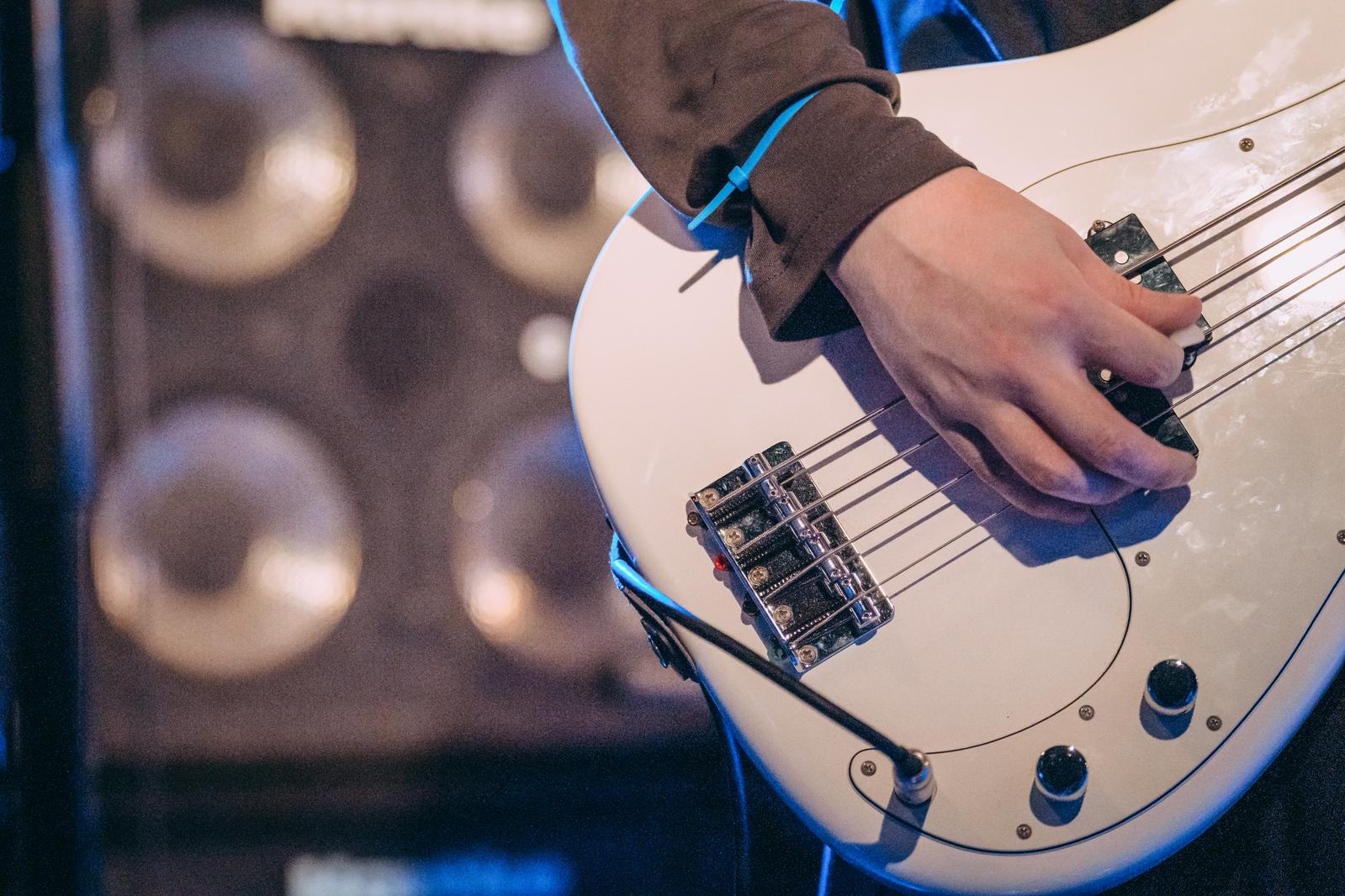 ライブステージで白いベースギターを弾くベーシストの腕と結束バンド