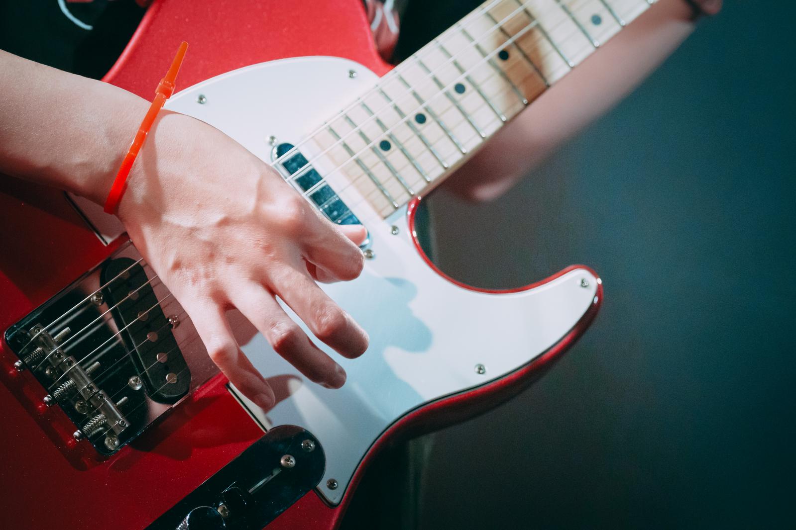 赤いギターを弾く人の腕に巻かれた結束バンドをアップで撮影した写真
