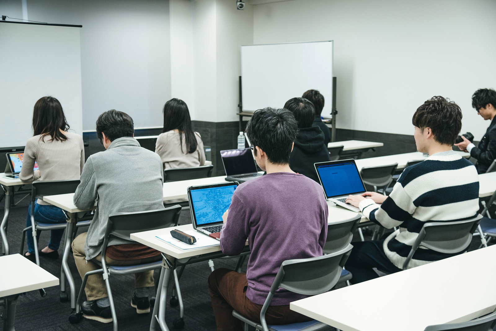 セミナー会場で机に着席している複数の参加者とスクリーン