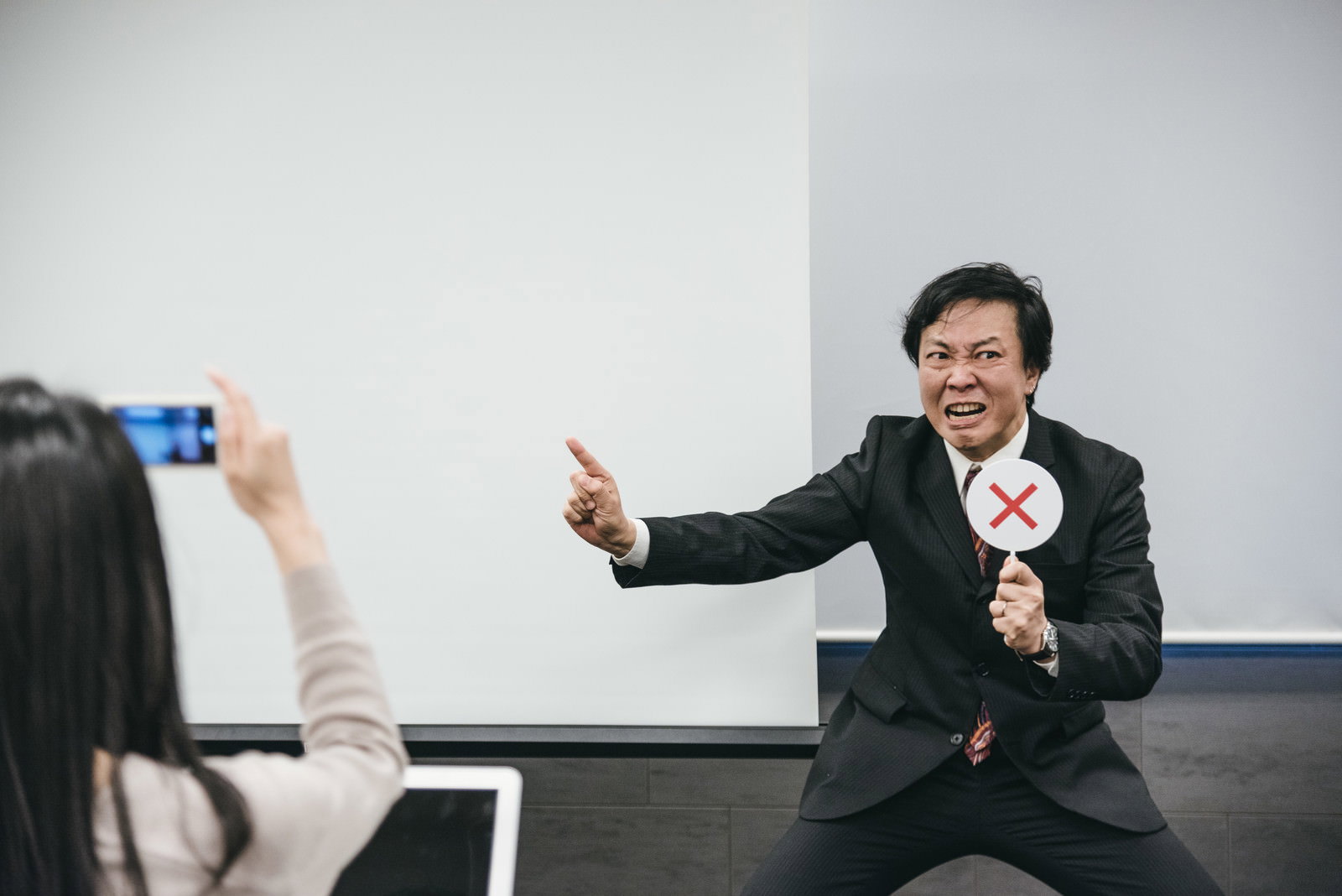 会議室で指差しポーズを取る黒いスーツ姿の男性［モデル：のせさん］
