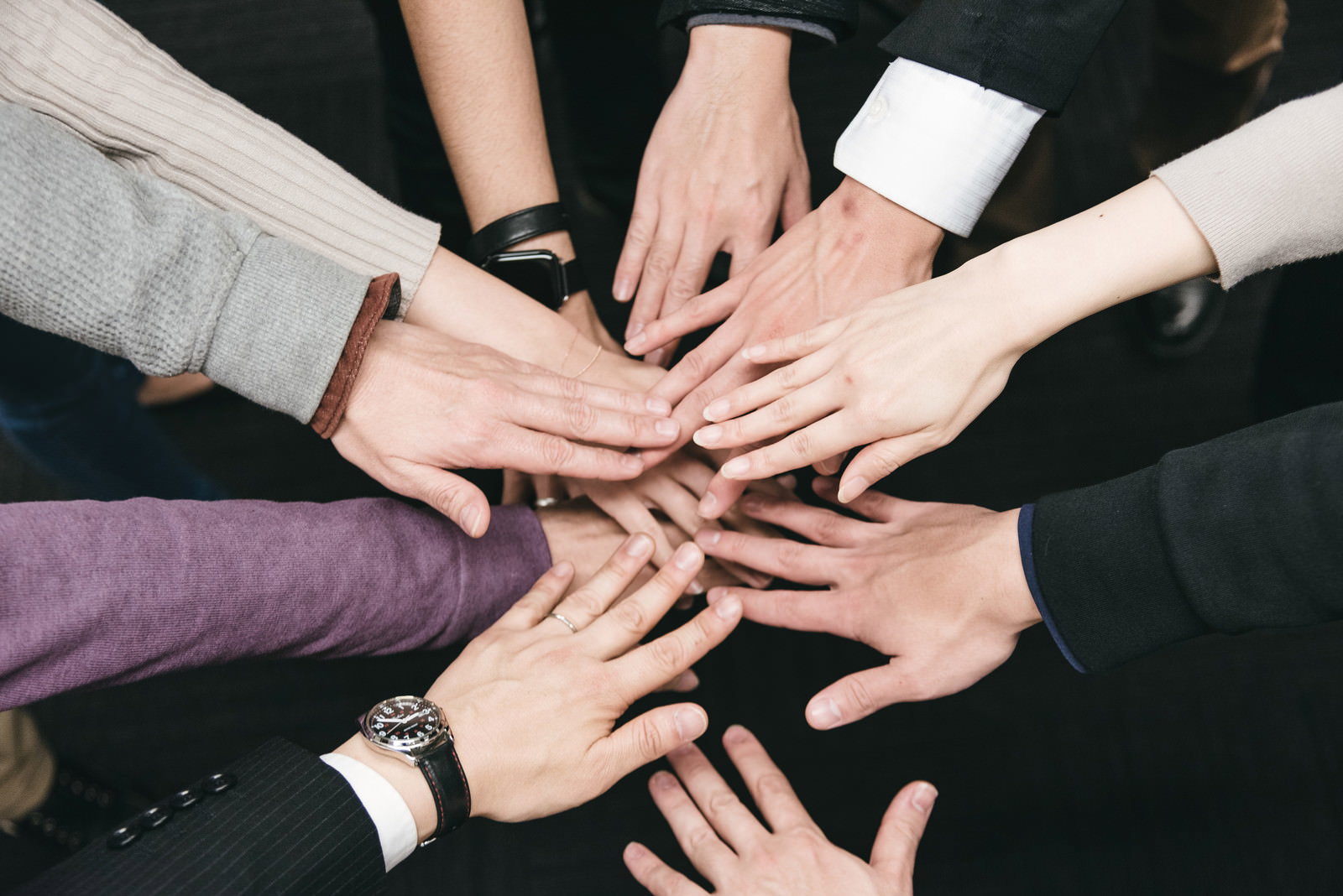 多くの人が手を中央に重ね合わせてチームワークを示している様子