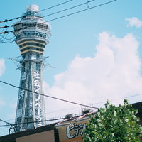 青空に白い雲と電線越しに見上げる通天閣の街角風景の写真