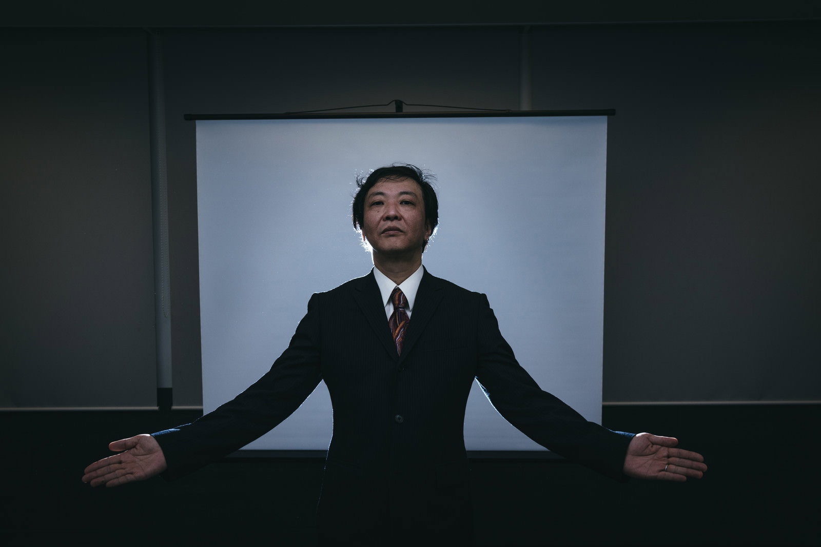 スーツを着た男性が両手を広げてセミナーを行っている様子［モデル：のせさん］