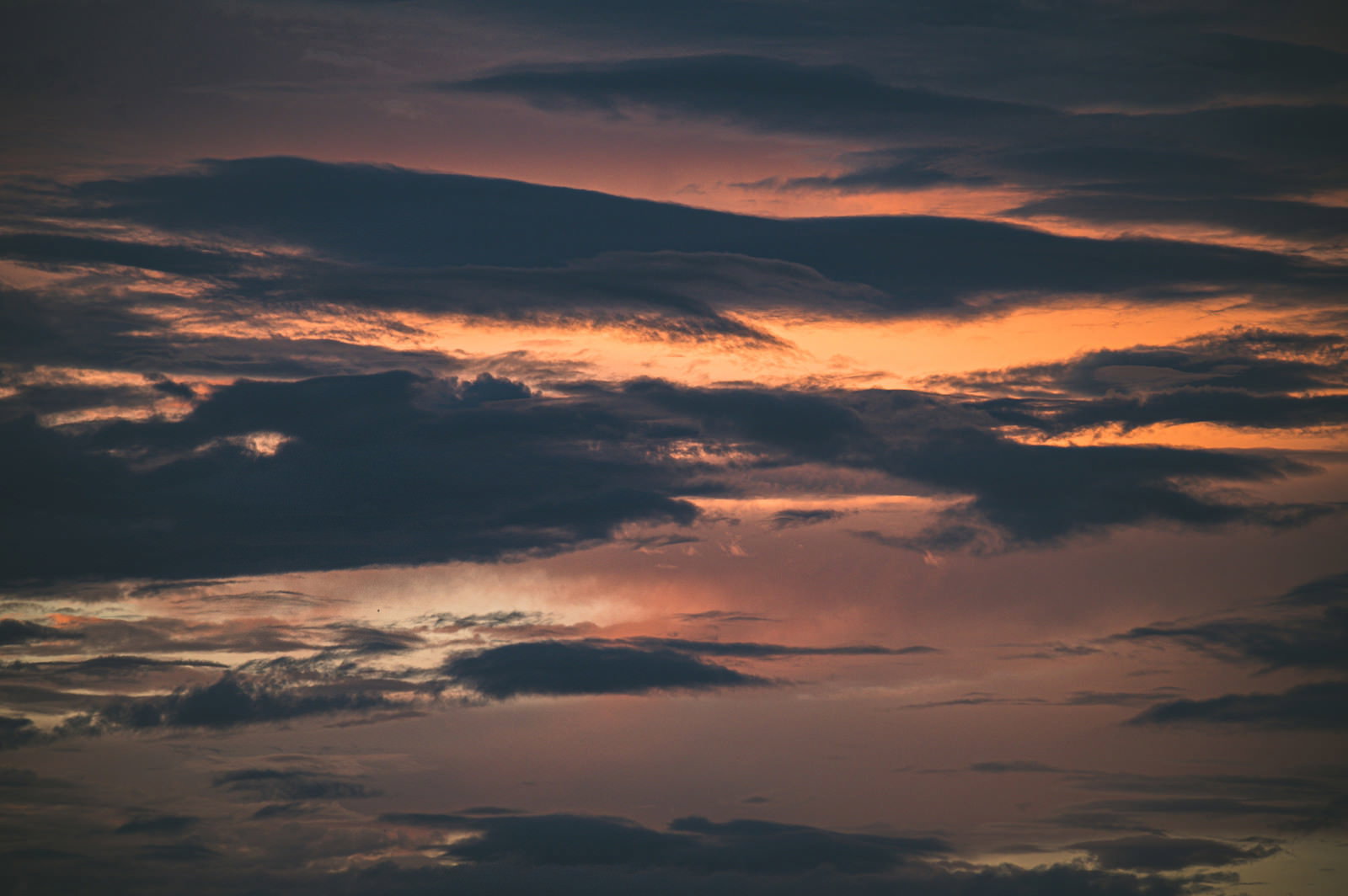 オレンジ色の夕焼け空に浮かぶ暗いシルエットの雲