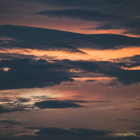 夕焼けの空を遮る黒い雲のシルエット、オレンジ色のグラデーション背景の写真