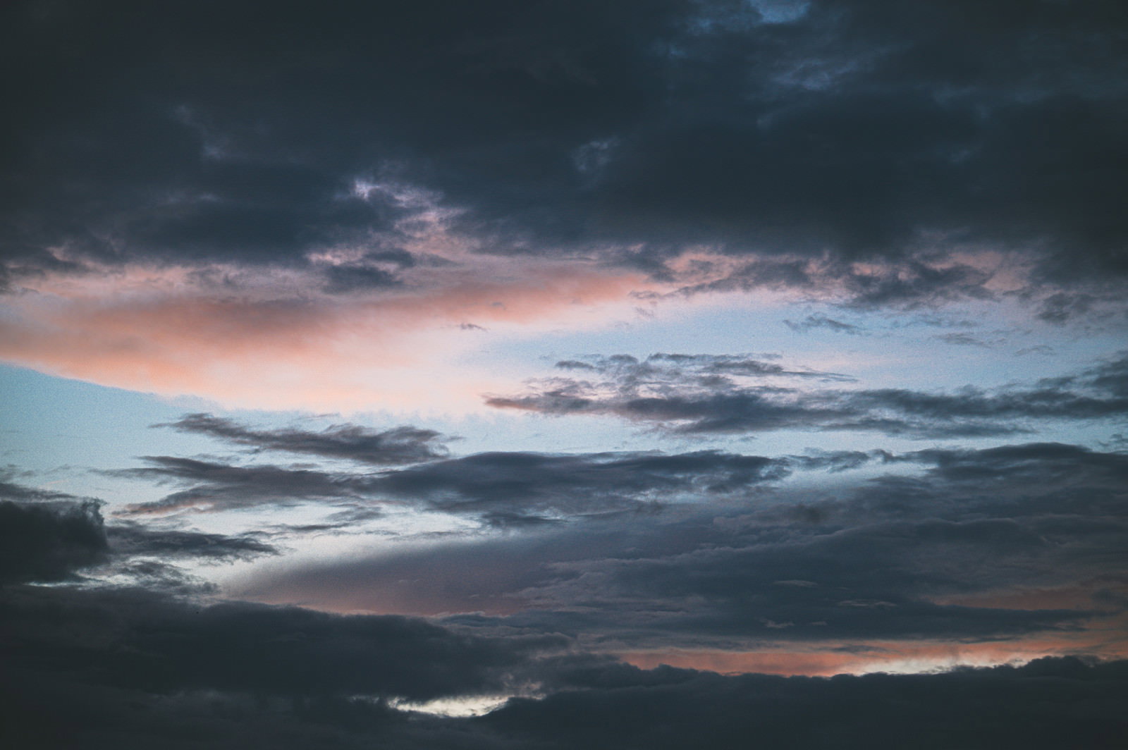 厚い黒い雲の合間から青い空と夕焼けの色彩が見える劇的な空模様