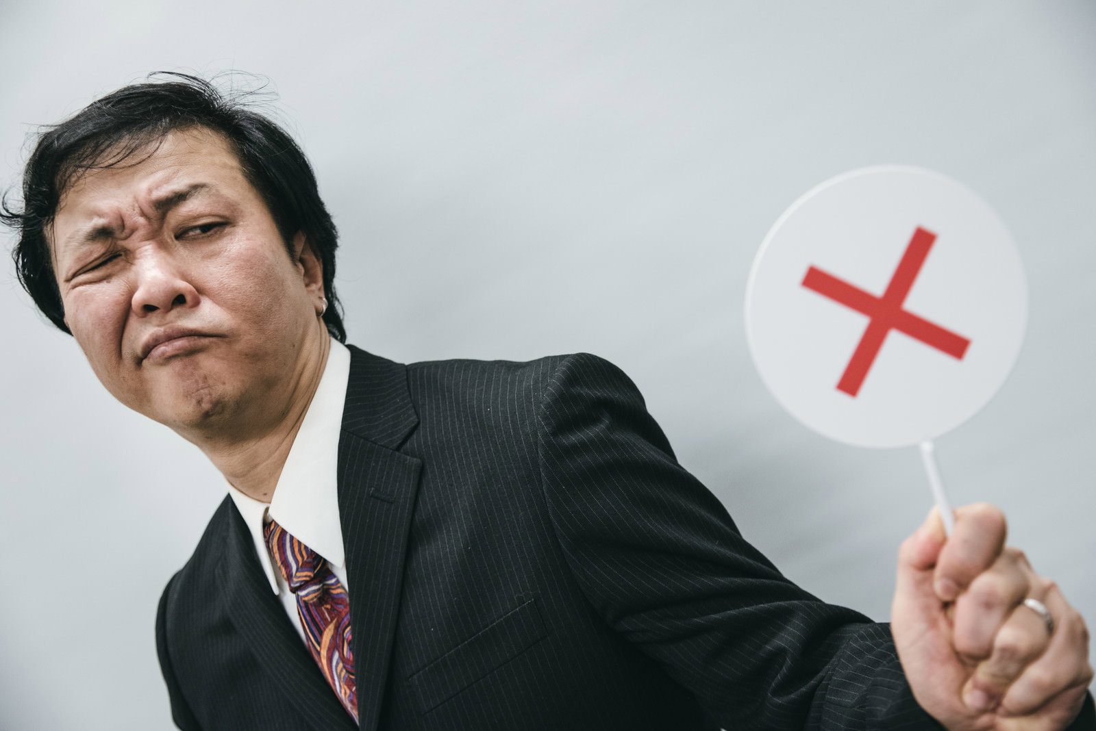 白いバツ印の札を持って不正解を示すスーツ姿の男性［モデル：のせさん］