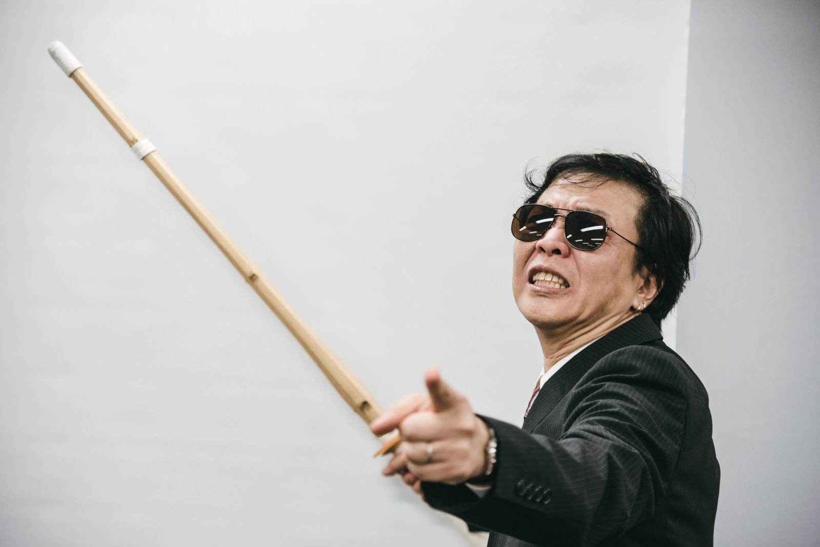 サングラスをかけて竹刀を持つ威圧的な表情の男性講師［モデル：のせさん］