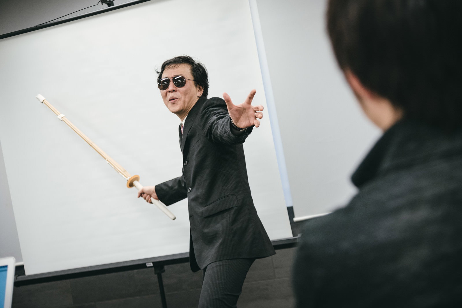 竹刀を持った男性講師がホワイトボードの前で指導している様子［モデル：のせさん］