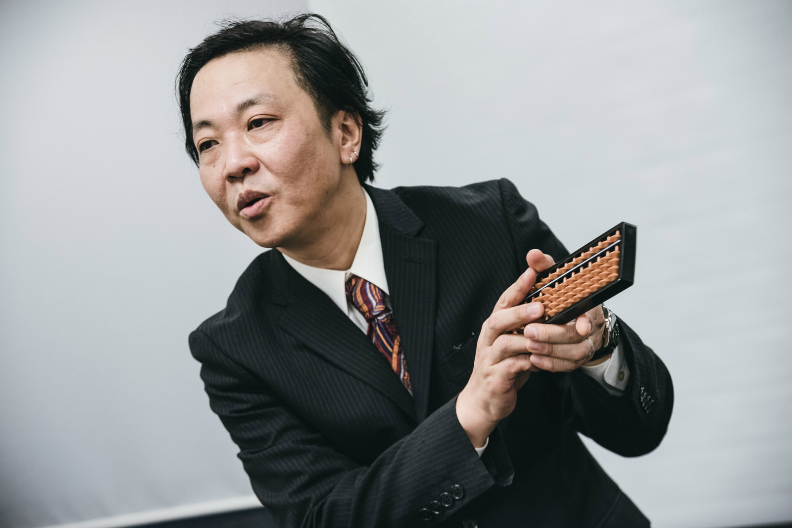 そろばんを両手で持つスーツ姿の営業マンの男性［モデル：のせさん］
