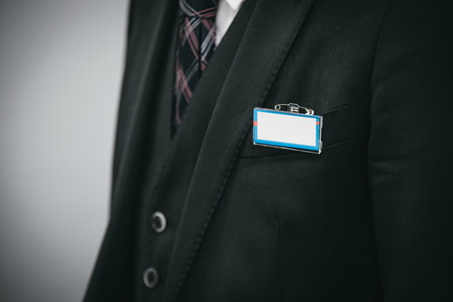スーツに青いネームカードをつける会社員の胸元