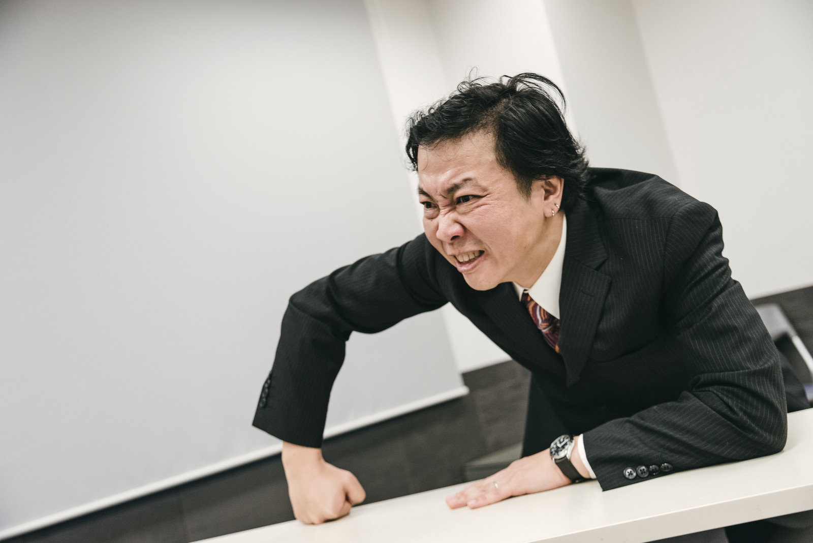会議室で机に手をついて激怒するスーツ姿の上司［モデル：のせさん］