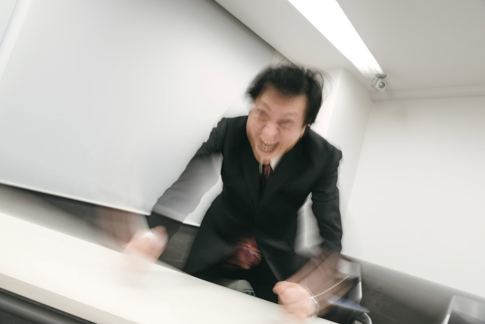 オフィスで大きく笑う黒いジャケット姿の男性［モデル：のせさん］