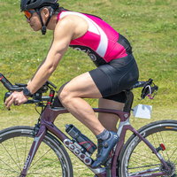 ピンクと黒のウェアのトライアスリートがロードバイクを運転するの写真