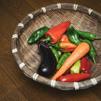 採れたての茄子と人参と唐辛子を竹製の笊に盛った収穫野菜の写真