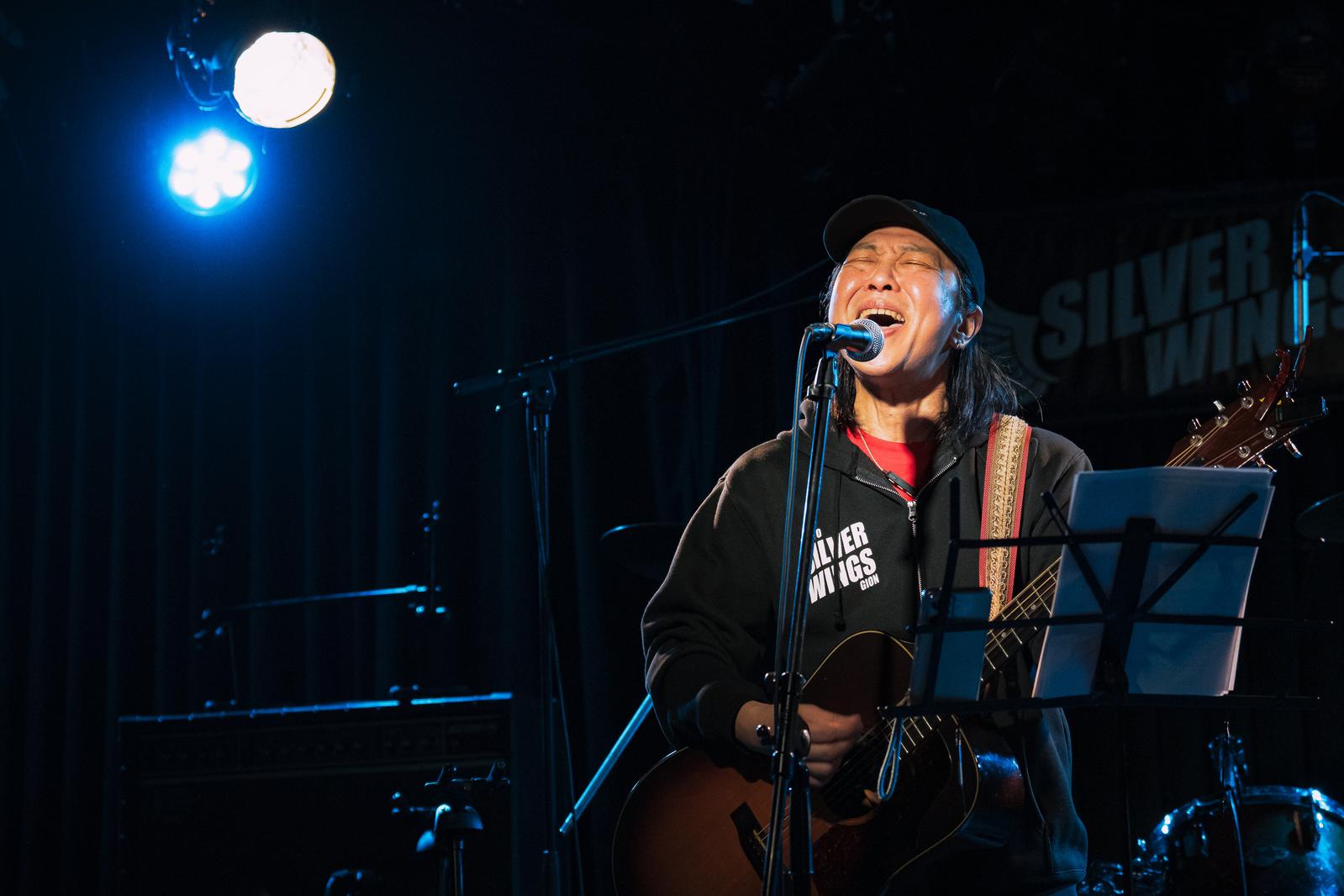 ライブハウスでギターを弾きながら熱唱する男性［モデル：のせさん］