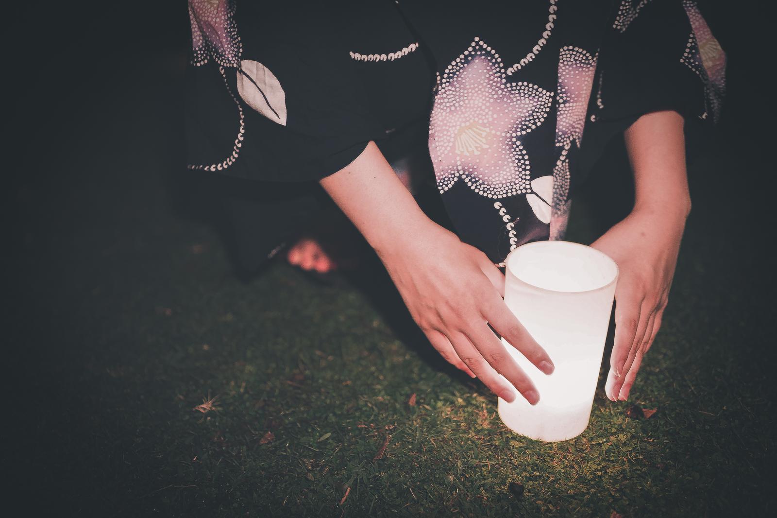 浴衣姿の女性が両手で白い灯籠を持ち、燈花会の会場で灯をともしている