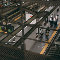 駅のホーム上で電車を待つため並ぶ乗客たちの写真