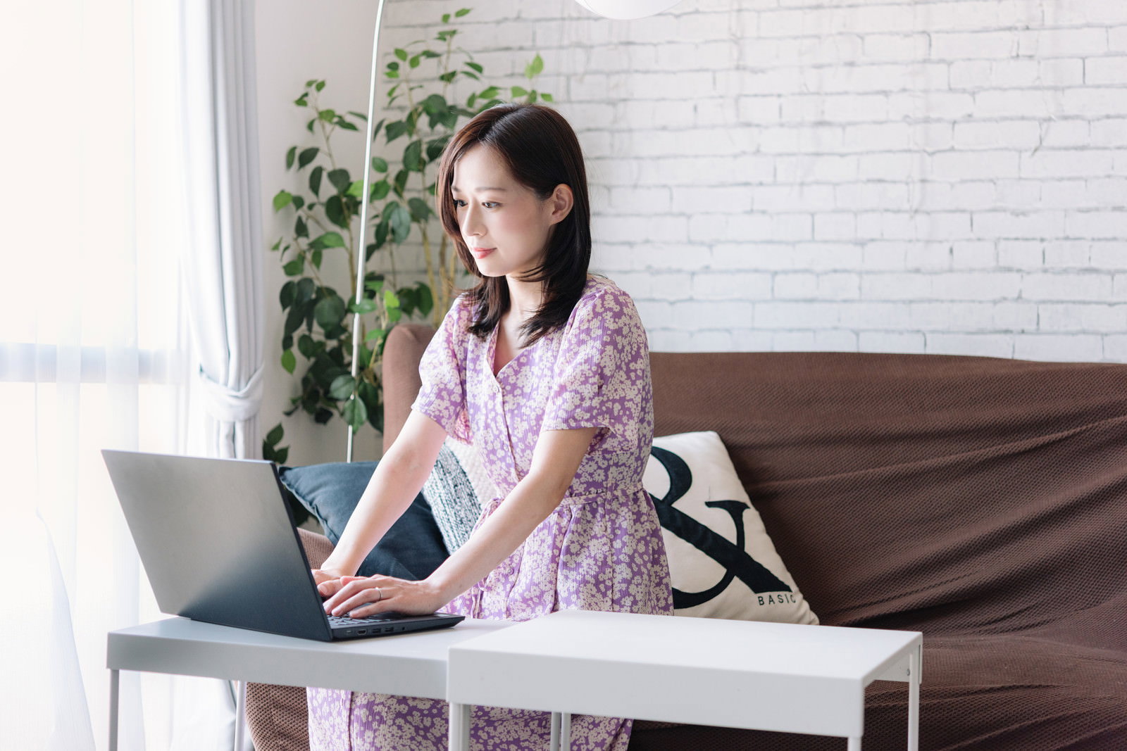 リビングの白いテーブルでノートパソコンを使ってテレワークする紫色の服を着た女性