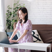 リビングの白いテーブルでノートパソコンを使ってテレワークする女性の写真