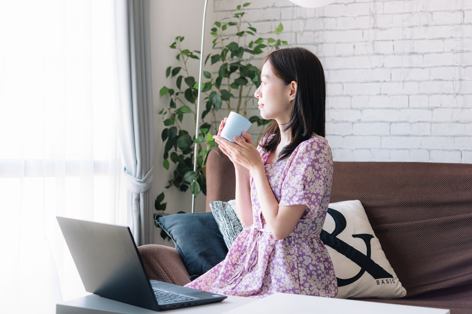 コーヒーを飲みながらノートパソコンで作業する女性
