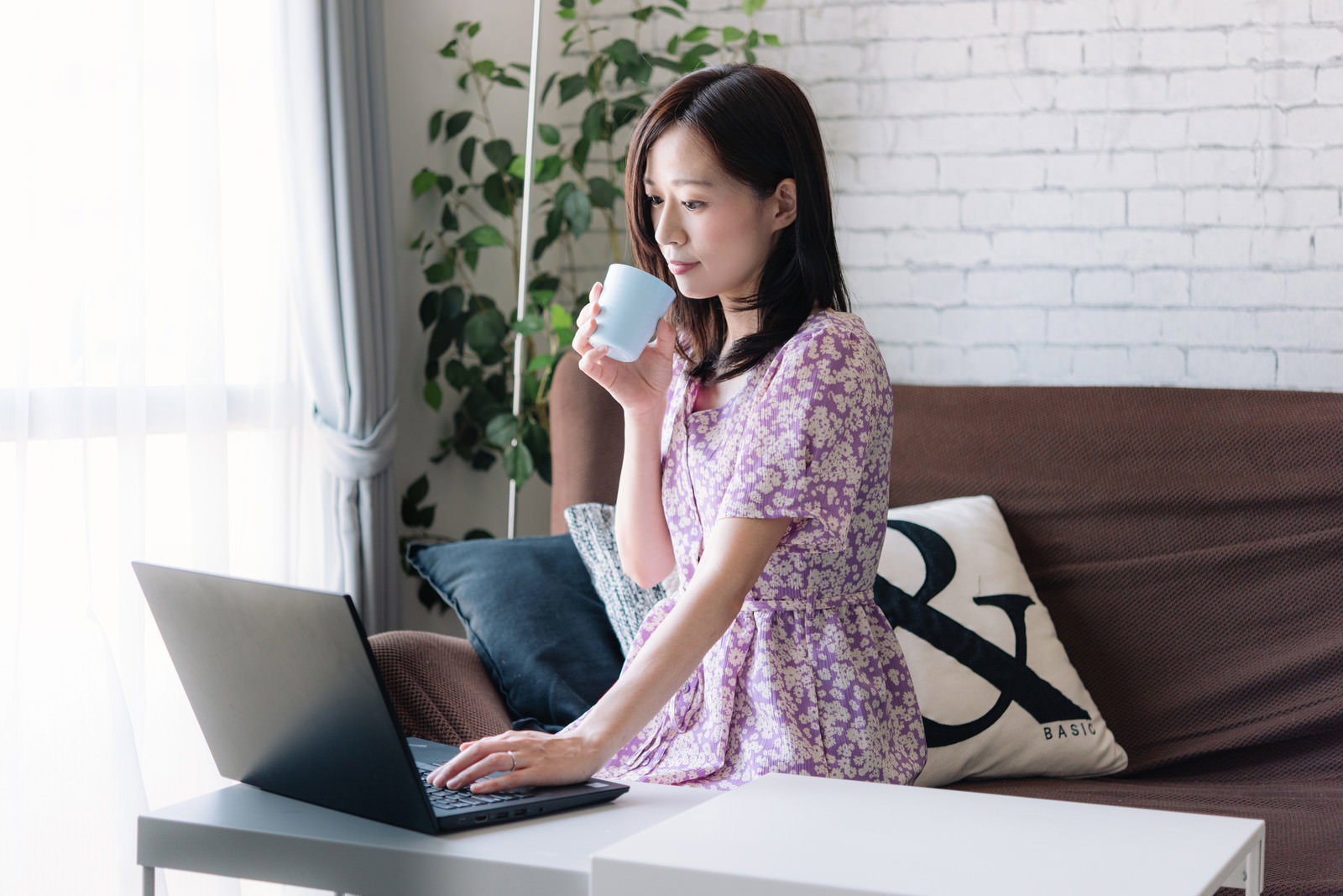 コーヒーカップを持ちながらノートパソコンで作業する女性