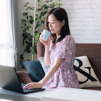 コーヒーを片手に在宅勤務中の女性がノートパソコンで業務を進めるの写真