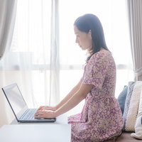 明るい室内で花柄ワンピースを着てテレワークする女性の写真